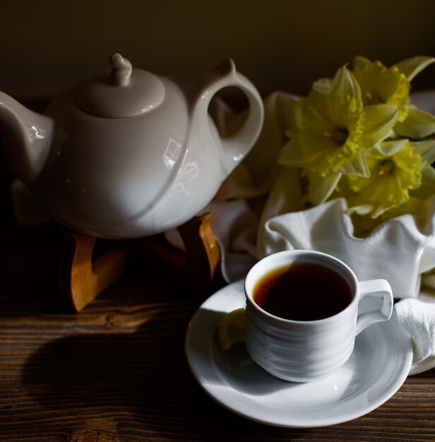 Una taza de té negro en una taza blanca junto a la tetera blanca