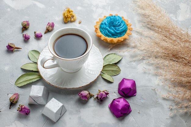 Taza de té con pastel de crema azul, caramelos de chocolate sobre blanco-gris, galletas dulces de té dulce