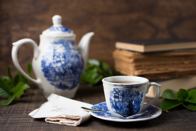 Taza de té de porcelana antigua y tetera con libros y servilleta doblada en mesa de madera