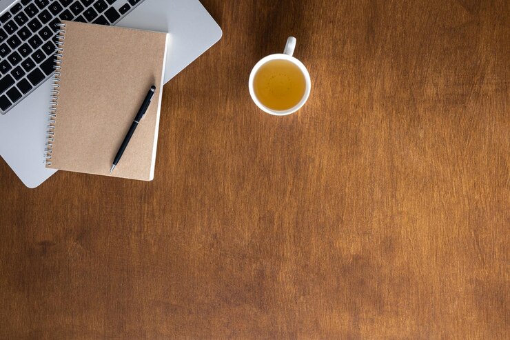 Foto gratuito taza de té de portátil y bloc de notas en una mesa de madera vista superior