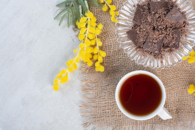 Taza de té y tazón de chocolate sobre arpillera con flores
