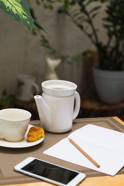 Taza de té con tetera y elementos de desayuno