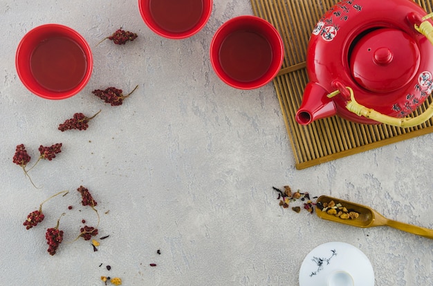 Taza y tetera asiáticas rojas con las hierbas en fondo gris texturizado