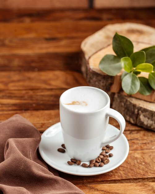 Una taza vacía blanca vista frontal con semillas de café marrón en la mesa de madera marrón semilla de taza de café
