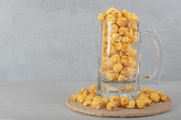 Taza de vidrio llena sobre un salvamanteles anillado con palomitas de maíz con sabor a caramelo en la mesa de mármol.