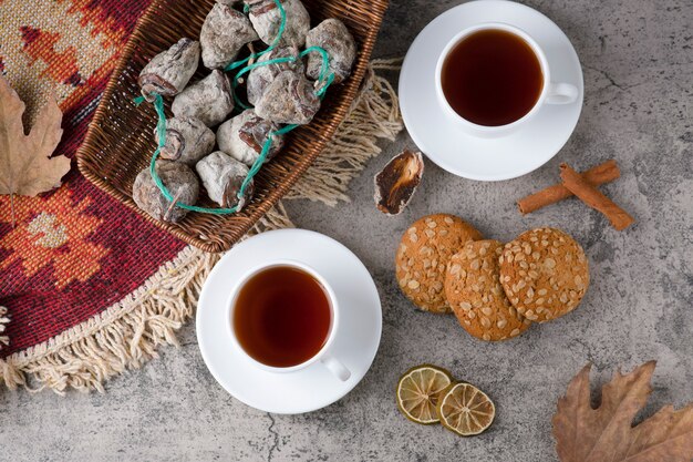 Tazas blancas de té caliente con frutos secos y galletas de avena en una mesa de piedra.