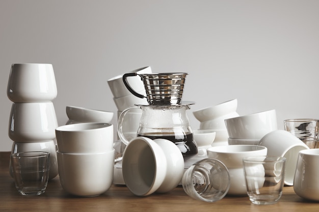 Tazas de café blancas y transparentes en blanco del caos en la mesa de madera gruesa. Cafetera de goteo con bebida filtrada en el centro.