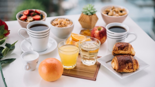 Tazas de café con bollos dulces y jugo en la mesa