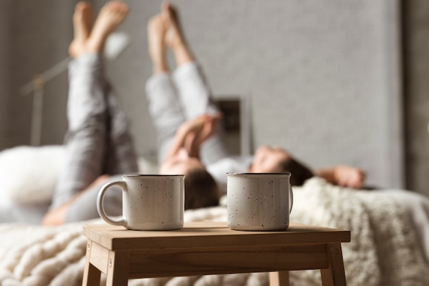 Tazas de café sobre la mesa con pareja detrás en la cama