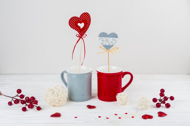 Tazas con corazones en varitas cerca de pequeños corazones y bayas