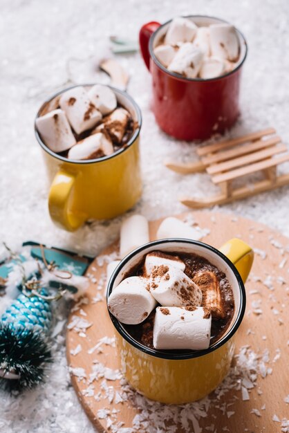 Tazas con dulces dulces y bebidas cerca de los juguetes de Navidad entre la nieve