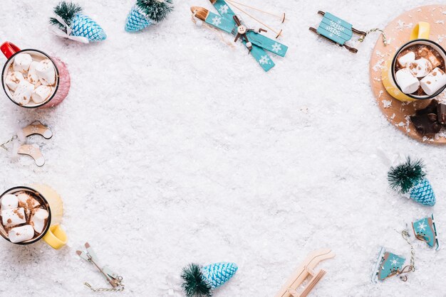 Tazas con malvaviscos y juguetes navideños sobre nieve.