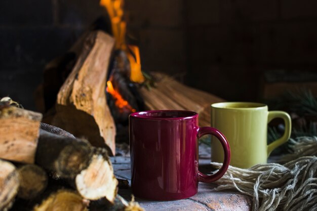 Tazas y manta junto a fuego en chimenea