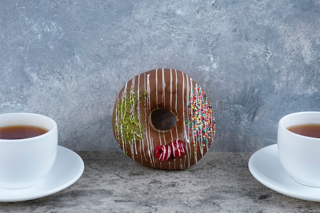 Foto gratuita tazas de té negro con donut helado de chocolate sobre mármol.