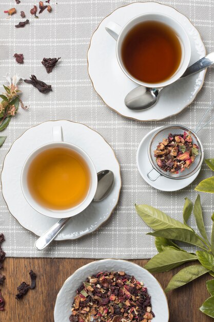 Tazas de té con sabor a hierbas de té secas en mantel de madera