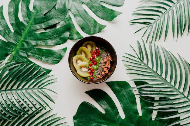 Tazón de acai con bayas saludables, kiwi, aguacate en hojas de palmeras tropicales. Comida vegetariana saludable.