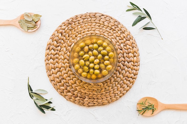 Tazón con aceitunas y aceite y hierbas sobre fondo blanco