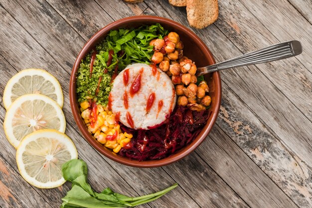 Tazón de arroz con verduras servido con rodajas de limones en tablero de madera