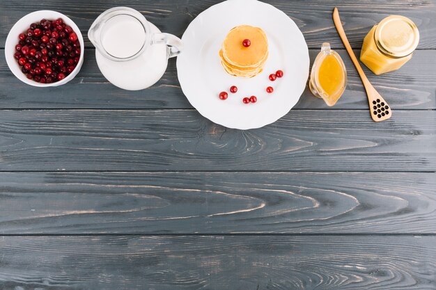 Tazón de bayas de grosellas rojas; Leche; Miel y panqueques sobre fondo de madera con textura