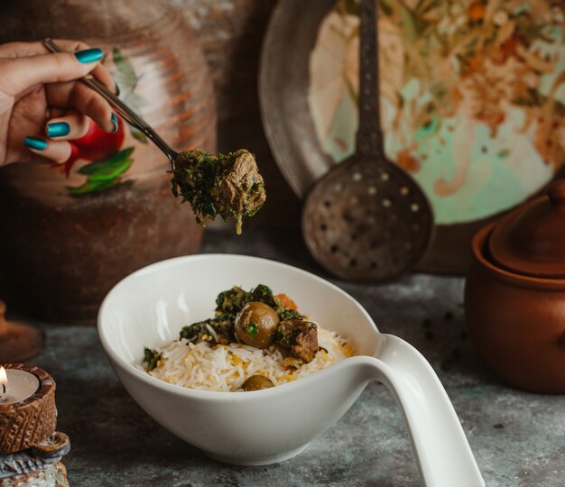 Un tazón blanco de govurma plov tradicional con frutos secos y castañas.