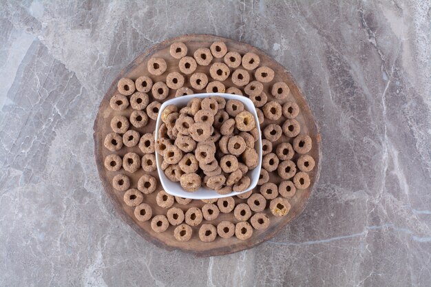 Un tazón blanco lleno de anillos de cereales de chocolate saludables en una pieza de madera.