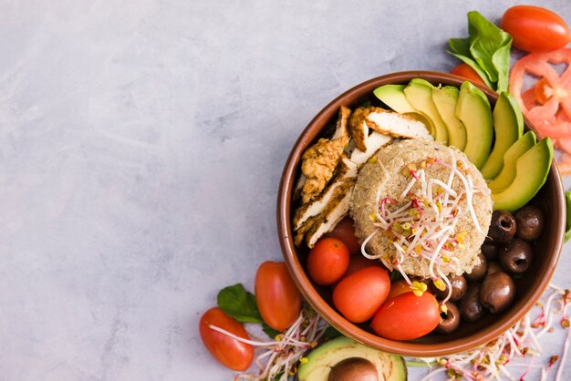 Tazón de burrito de pollo con arroz; brote; tomate; Aguacate y oliva sobre fondo de hormigón.