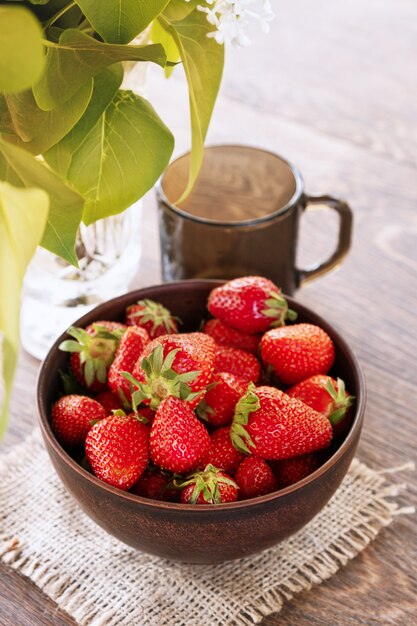 Tazón de cerámica de vidrio con fresas maduras fress y vidrio oscuro sobre una mesa.