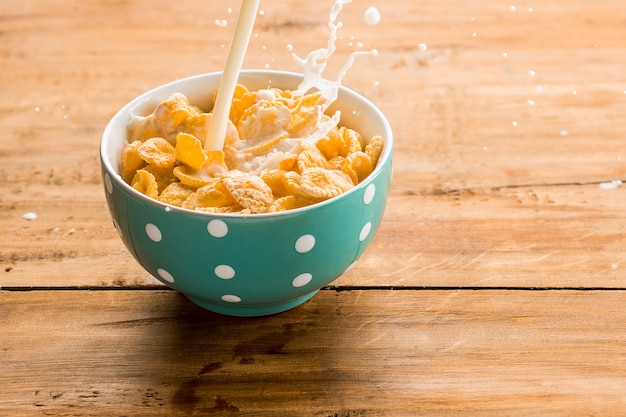 tazón de cereal con chorro de leche en la mesa de madera