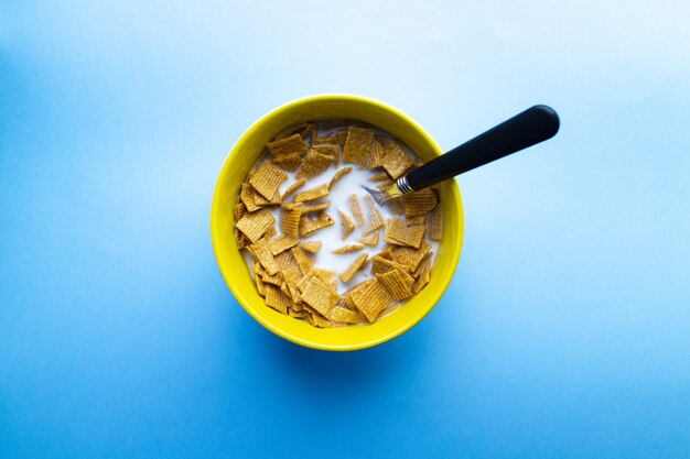 Tazón de cereal en trozos cuadrados con leche y cuchara en un tazón aislado