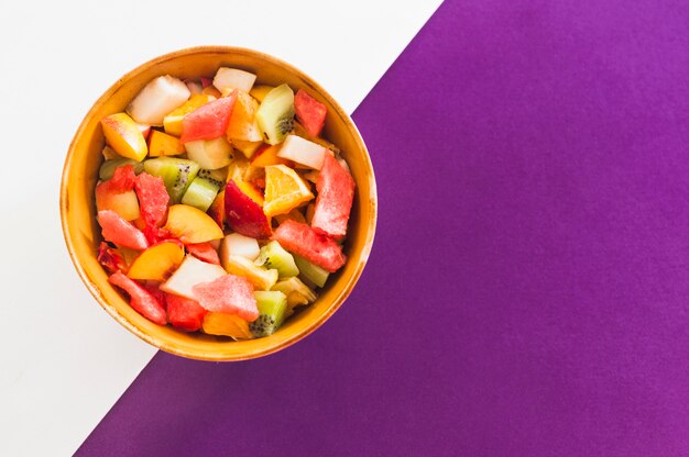 Tazón de ensalada de frutas sobre fondo blanco y púrpura