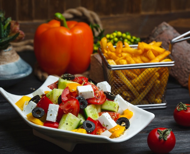 Tazón de ensalada griega adornada con pimiento amarillo, servido con papas fritas