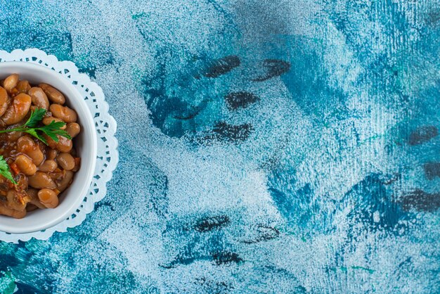 Un tazón de frijoles horneados en una montaña rusa, sobre la mesa azul.