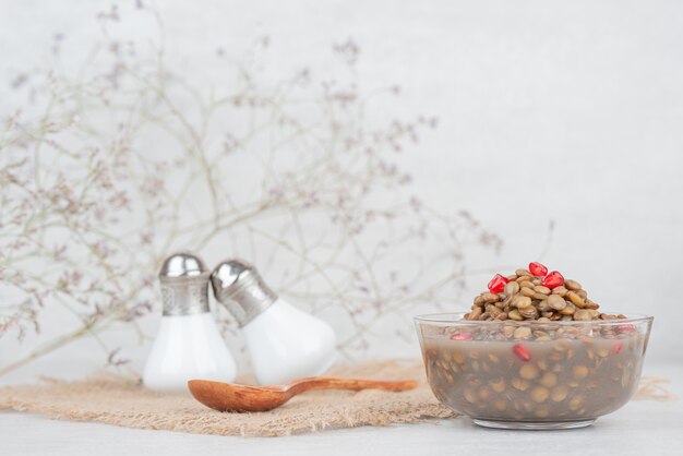 Tazón de frijoles con semillas de granada en mesa blanca
