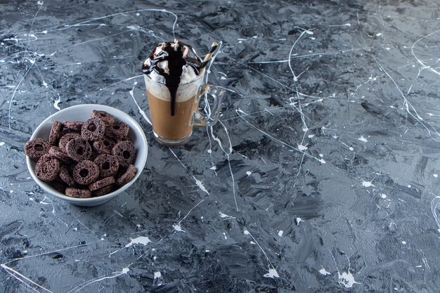 Tazón de fuente blanco de cereales de chocolate y vaso de café sobre la superficie de mármol.