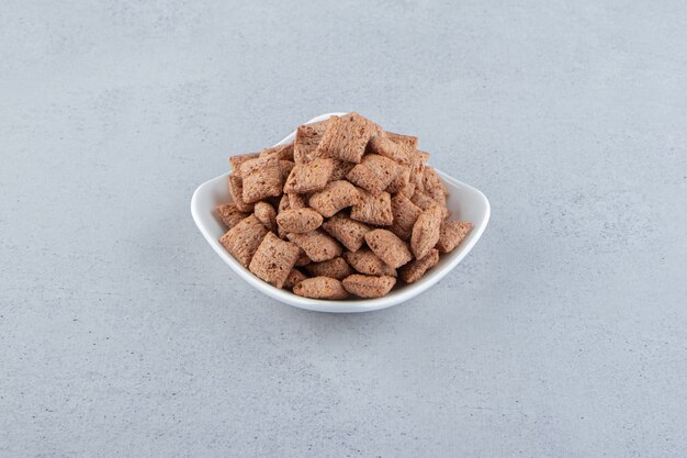 Tazón de fuente blanco de copos de maíz de almohadillas de chocolate sobre fondo de piedra. Foto de alta calidad