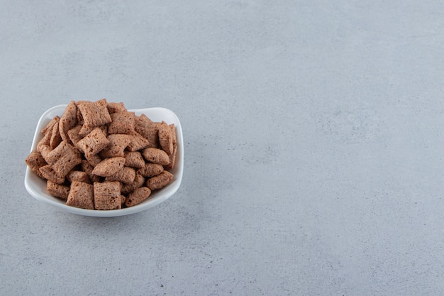 Tazón de fuente blanco de copos de maíz de almohadillas de chocolate sobre fondo de piedra. Foto de alta calidad