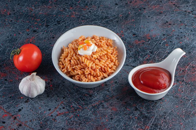 Tazón de fuente blanco de deliciosa pasta fusilli sobre superficie de mármol.