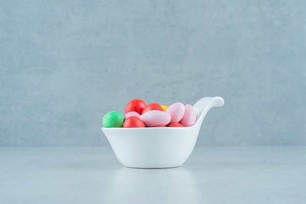 Un tazón de fuente blanco lleno de caramelos coloridos dulces redondos en el fondo blanco. Foto de alta calidad