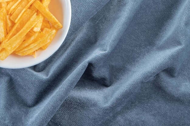 Tazón de fuente blanco de palitos de patata crujientes sobre tela azul.