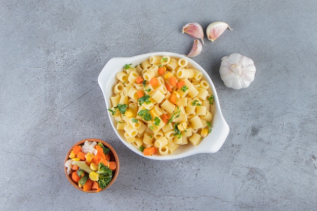 Tazón de fuente blanco de pasta deliciosa con ensalada fresca sobre fondo de piedra.