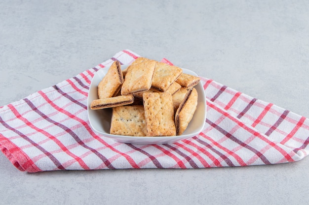 Tazón de fuente blanco de sabrosas galletas crujientes sobre fondo de piedra.