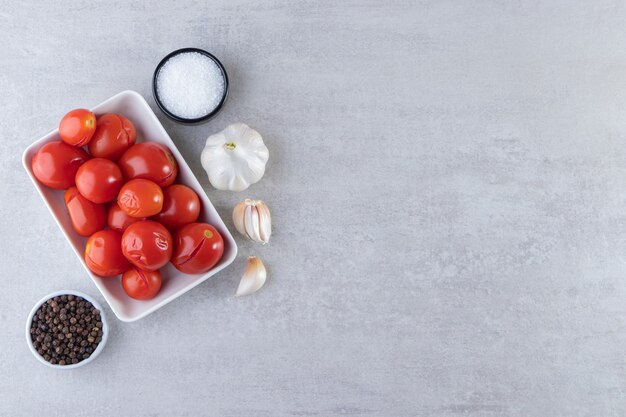 Tazón de fuente blanco de tomates encurtidos colocados sobre fondo de piedra.