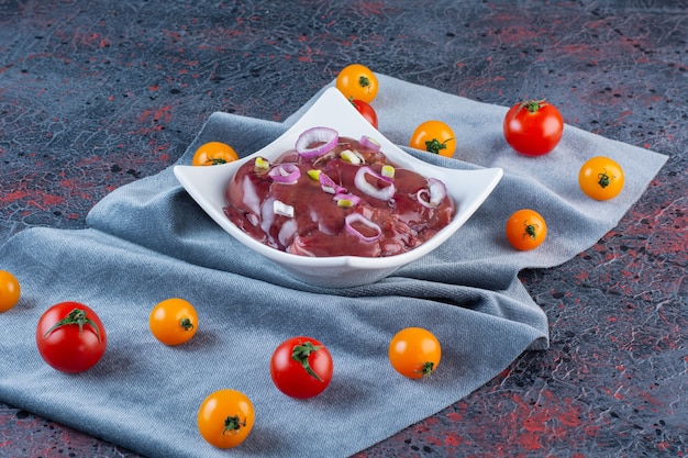 Foto gratuita tazón de fuente blanco de trozos de carne con tomates cherry sobre fondo de mármol.