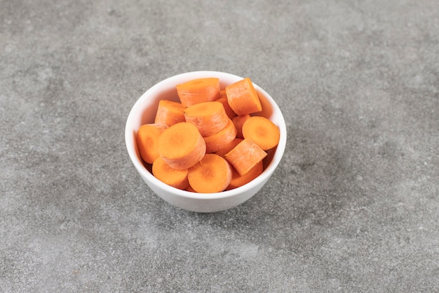 Tazón de fuente blanco de zanahorias frescas en rodajas sobre la superficie de mármol.