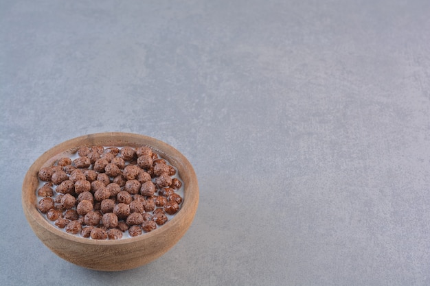 Tazón de fuente de bolas de cereal de chocolate con leche sobre fondo de piedra.