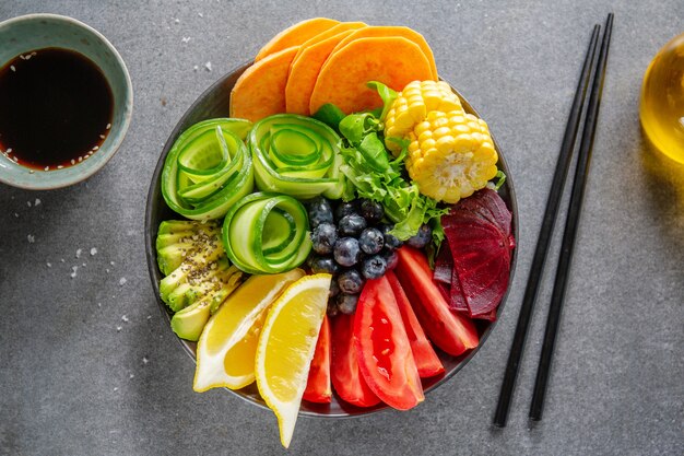 Tazón de fuente de Buda vegano con verduras y frutas servido en un tazón sobre fondo gris. De cerca