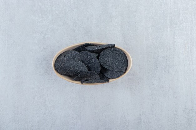 Tazón de fuente de chips negros crujientes salados en piedra.