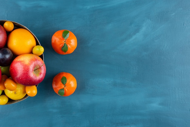 Tazón de fuente de diversas frutas frescas colocadas sobre fondo azul.