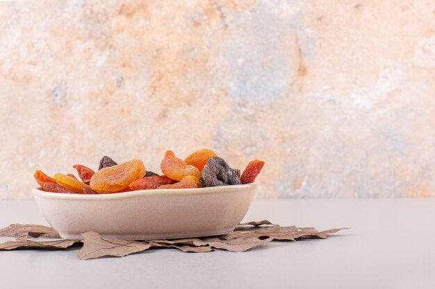 Tazón de fuente de diversas frutas orgánicas con hojas secas sobre fondo blanco. Foto de alta calidad