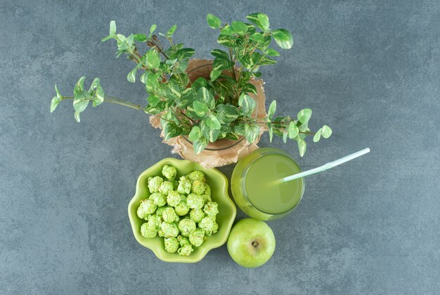 Tazón de fuente de dulces de palomitas de maíz, vaso de jugo de manzana, una sola manzana y un wase envuelto con una planta decorativa sobre fondo de mármol. Foto de alta calidad